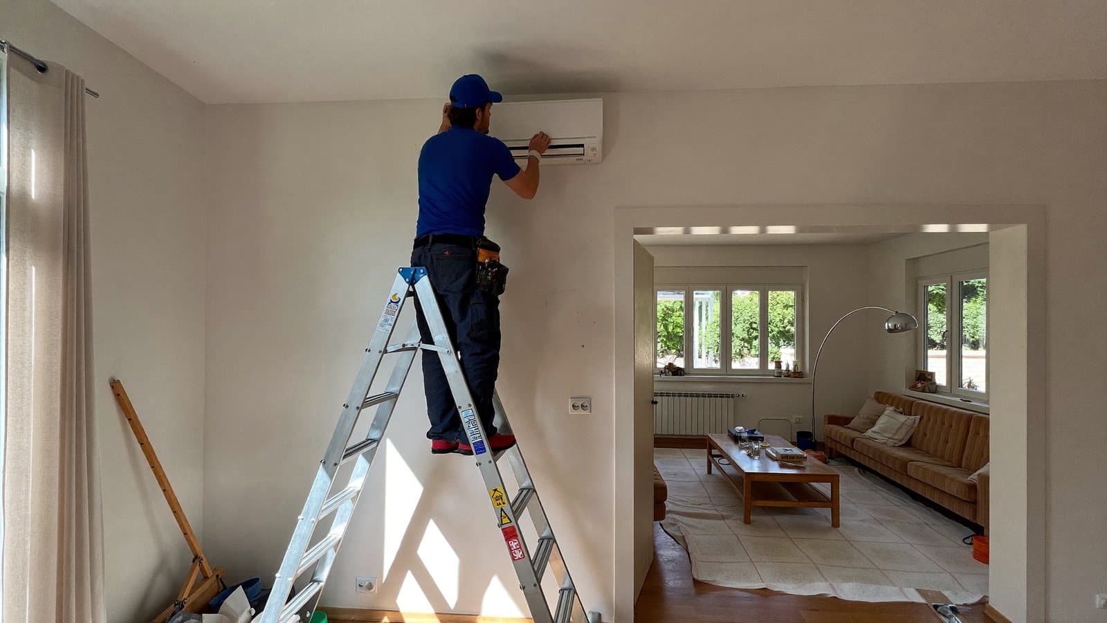 Tecnico su scala che fissa l'unità interna di un climatizzatore in un soggiorno